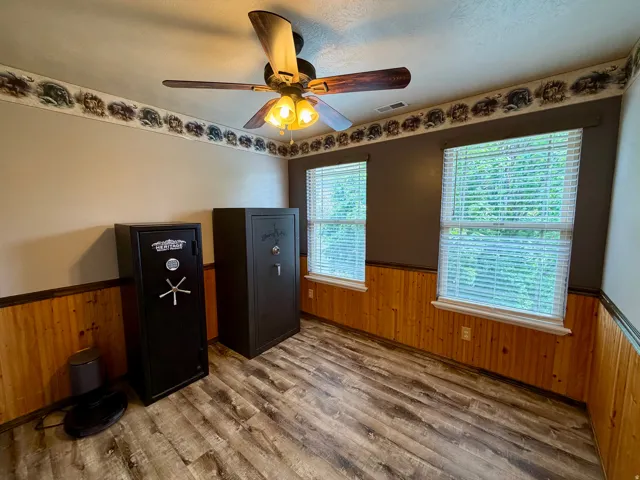 Room featuring wood-finish flooring, natural wood wainscoting, and a ceiling fan with integrated lighting