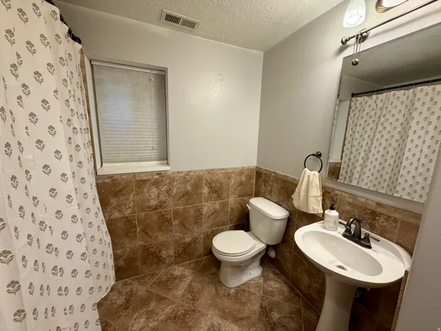 Bathroom featuring a pedestal sink with a dark-toned faucet, wall-mounted mirror, and vanity light fixture