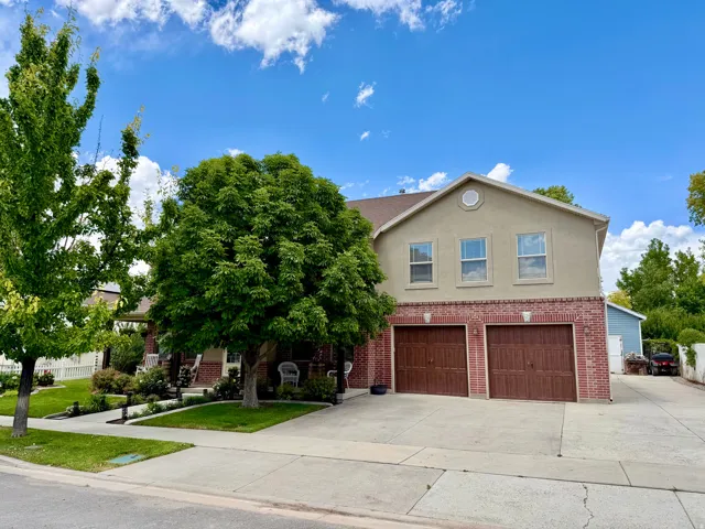 Two-story residence featuring a brick and stucco exterior, a two-car attached garage with wood-finish doors, and mature trees providing shade