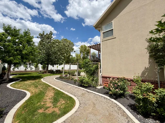 Landscaped backyard featuring a meandering gravel pathway, manicured lawn, and mature trees