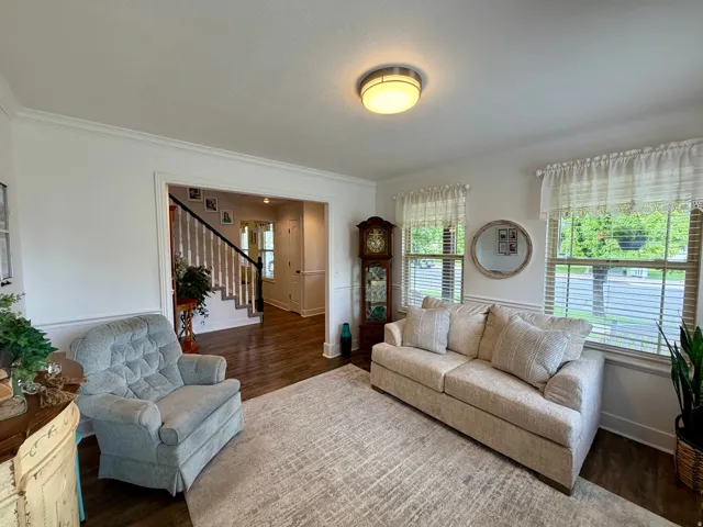 Spacious living area featuring wood-finish flooring, two large windows with blinds, and white wall trim