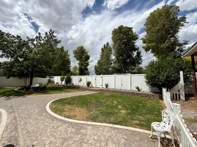 Spacious outdoor area with a white vinyl fence, mature trees, and a manicured lawn