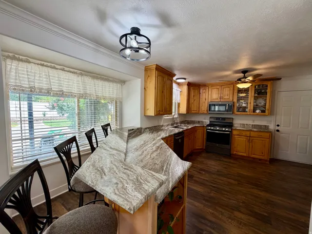 Kitchen featuring wood-finish flooring, light wood cabinetry, and a wraparound breakfast bar with a patterned countertop