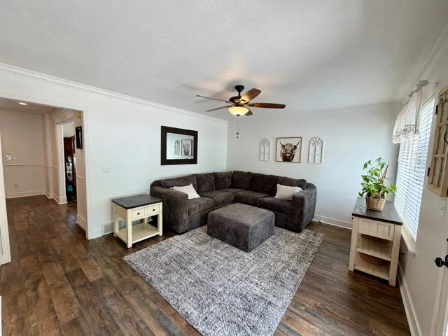 Spacious living area featuring wood-finish flooring, white baseboards, and crown molding