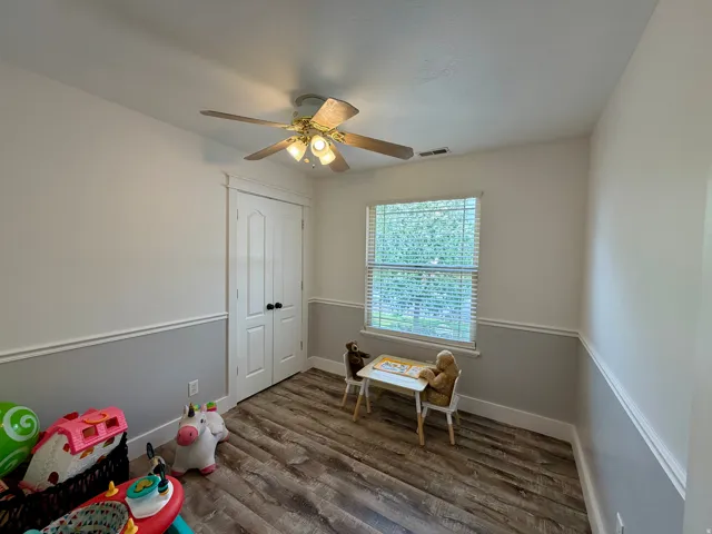 Room featuring wood-finish flooring, two-tone painted walls with chair rail molding, and a ceiling fan with integrated lighting