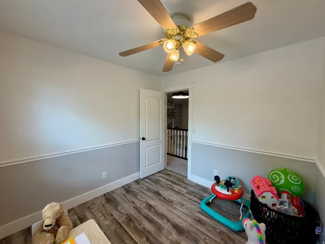 Room featuring wood-finish flooring, two-tone painted walls with chair rail molding, and a ceiling fan with integrated lighting