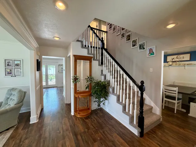 Inviting entryway with wood-finish flooring, a carpeted staircase featuring white balusters and a dark newel post, recessed lighting, and white wall trim
