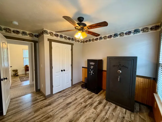 Room featuring wood-finish flooring, a ceiling fan with light fixture, and white bi-fold closet doors