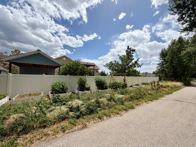 Backyard area featuring a white privacy fence, multiple raised garden beds, and mature trees