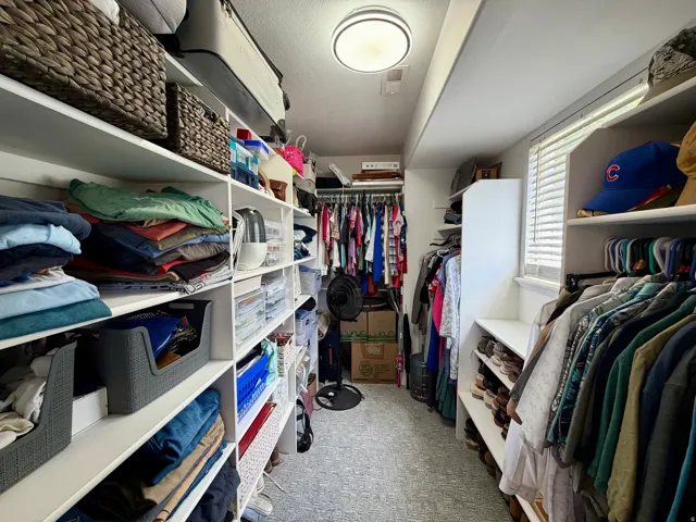 Custom closet featuring extensive built-in shelving, multiple hanging rods, and a window with blinds