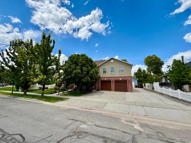 Two-story residence featuring a brick and stucco facade, dual garage doors, and a front lawn with mature trees