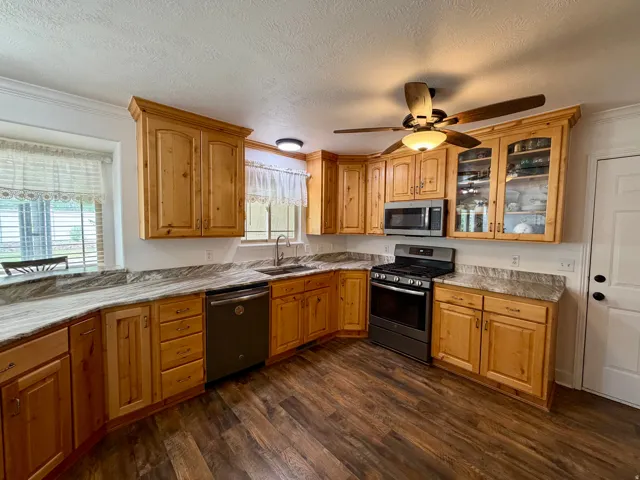 Kitchen featuring wood-finish cabinetry, light-toned countertops, stainless steel appliances, wood-finish flooring, and a ceiling fan with integrated lighting