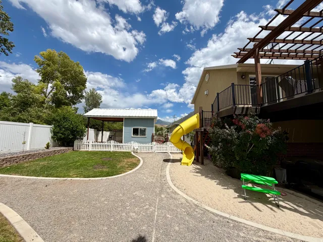 Spacious backyard featuring a multi-level deck with a pergola, a yellow spiral slide, and a sand play area