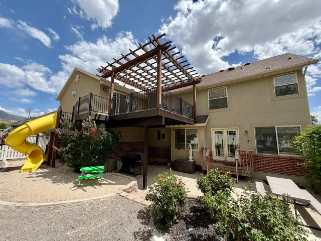Two-story exterior with a deck featuring a wooden pergola and black metal railings