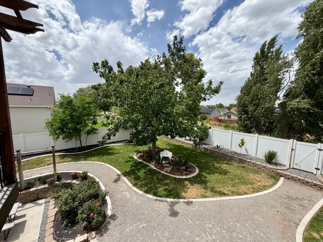 Expansive backyard featuring a large central tree, manicured lawn, gravel pathways, and white privacy fencing