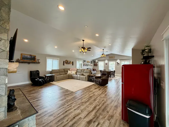 Spacious living area featuring wood-finish flooring, a stone-clad fireplace with hearth, recessed lighting, and multiple windows