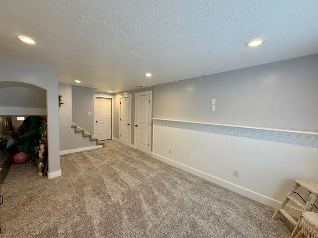 Spacious room featuring neutral carpeting, recessed lighting, white wainscoting, and white trim