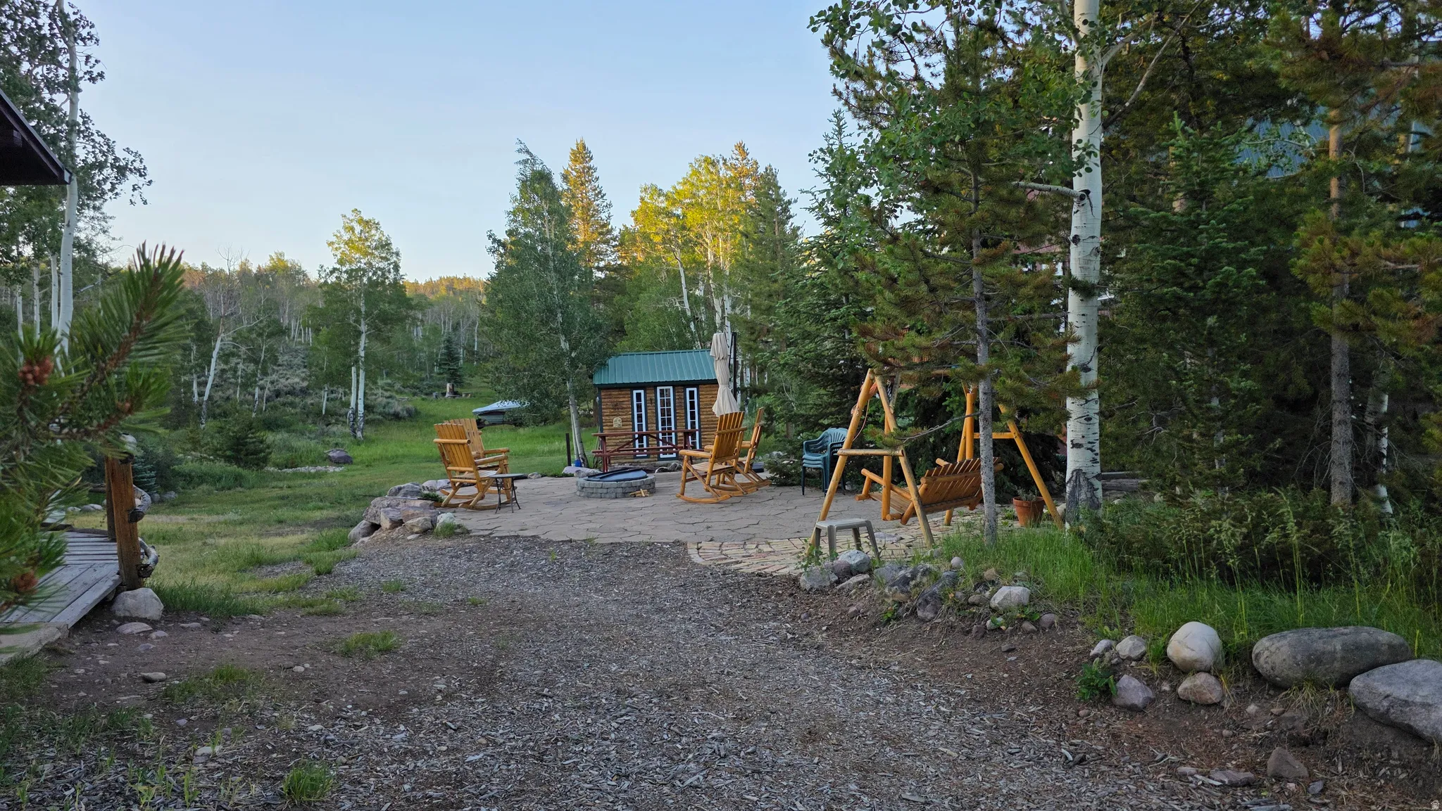 Expansive outdoor space featuring a graveled area, a separate patio with a fire pit, and a backdrop of mature trees
