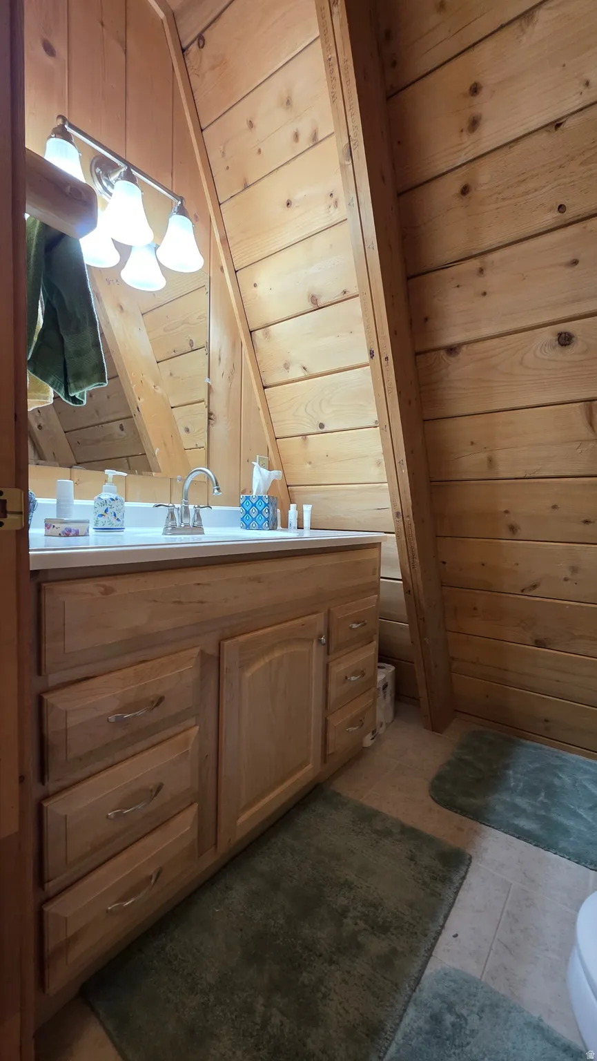 Wood-paneled bathroom featuring a light wood-finish vanity with multiple drawers and a cabinet, a white countertop, and a vanity mirror with a four-light fixture