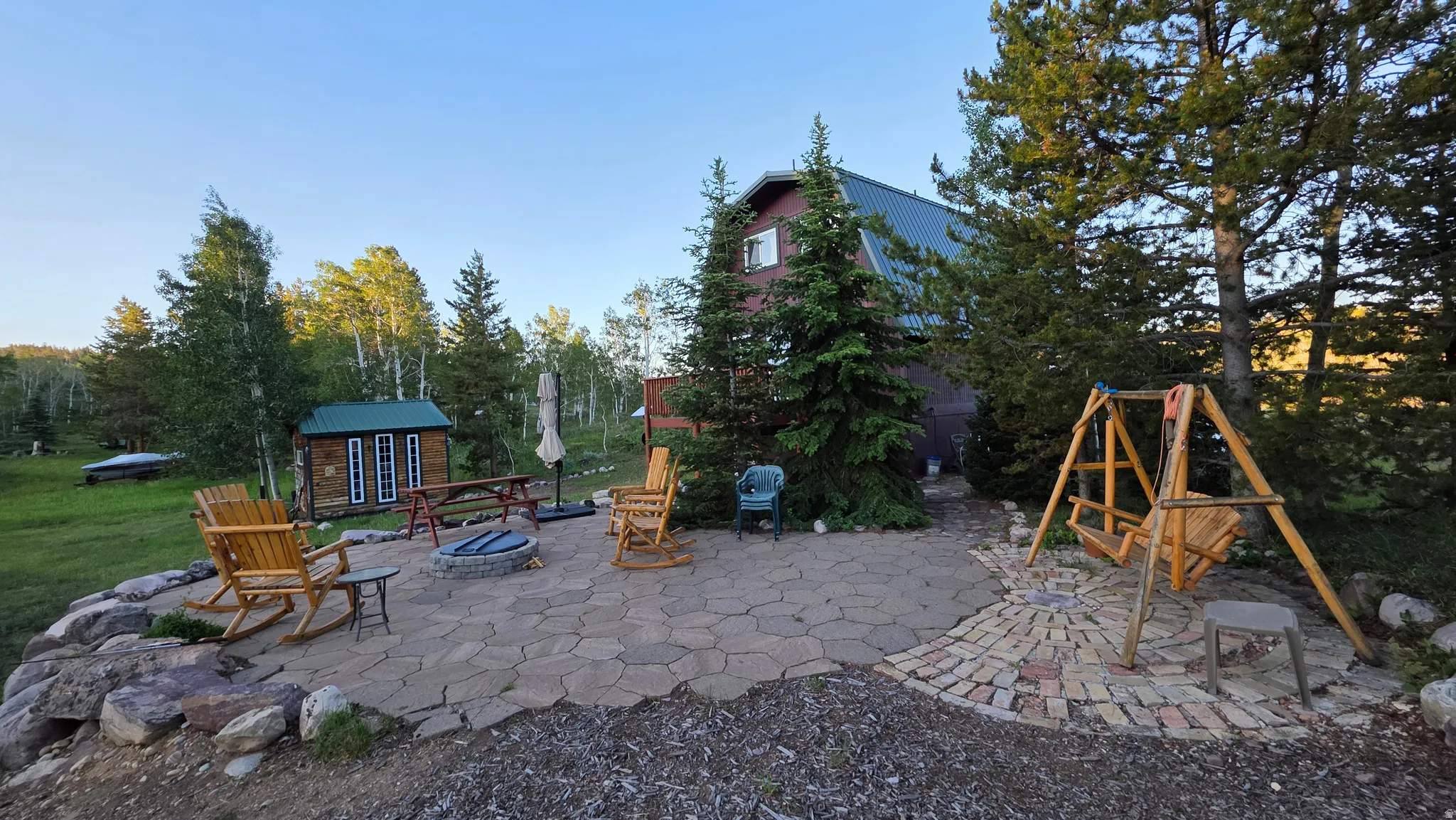 Expansive outdoor living area featuring a flagstone patio, integrated fire pit, and mature trees