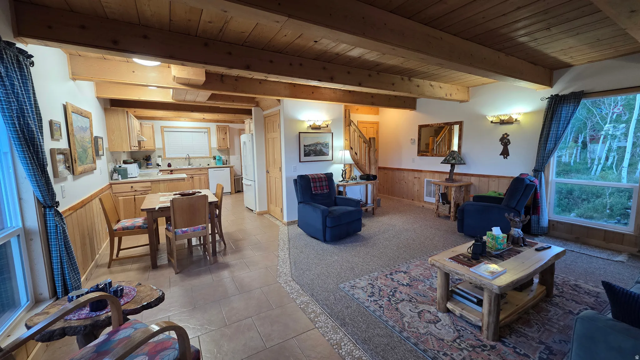 Open concept living space featuring a beamed wood ceiling, wood-paneled walls, and a large picture window