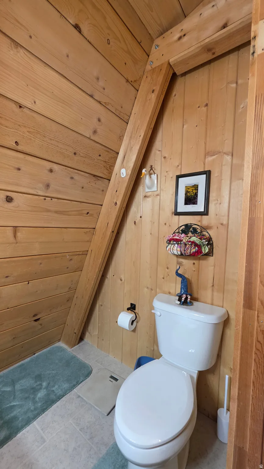 Wood-paneled bathroom featuring a white toilet, light-toned floor tiles, and a natural wood beam