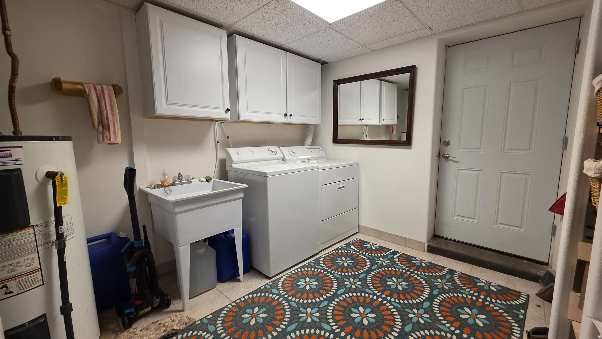 Dedicated utility area featuring a wall-mounted sink, upper cabinetry, and light-toned tile flooring