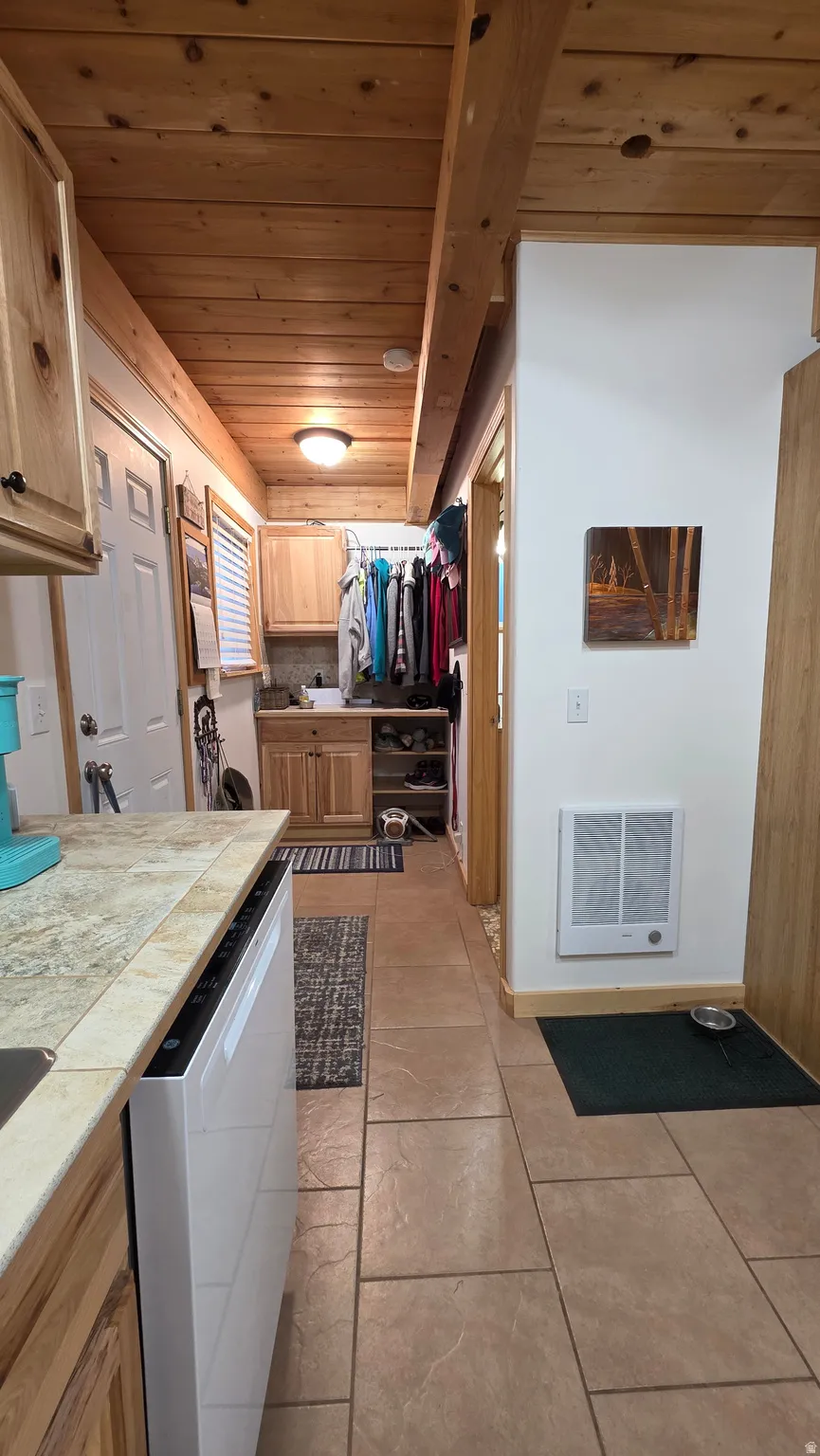 Kitchen area featuring a wood-panel ceiling with exposed beams, tile flooring, and a dishwasher integrated into the cabinetry