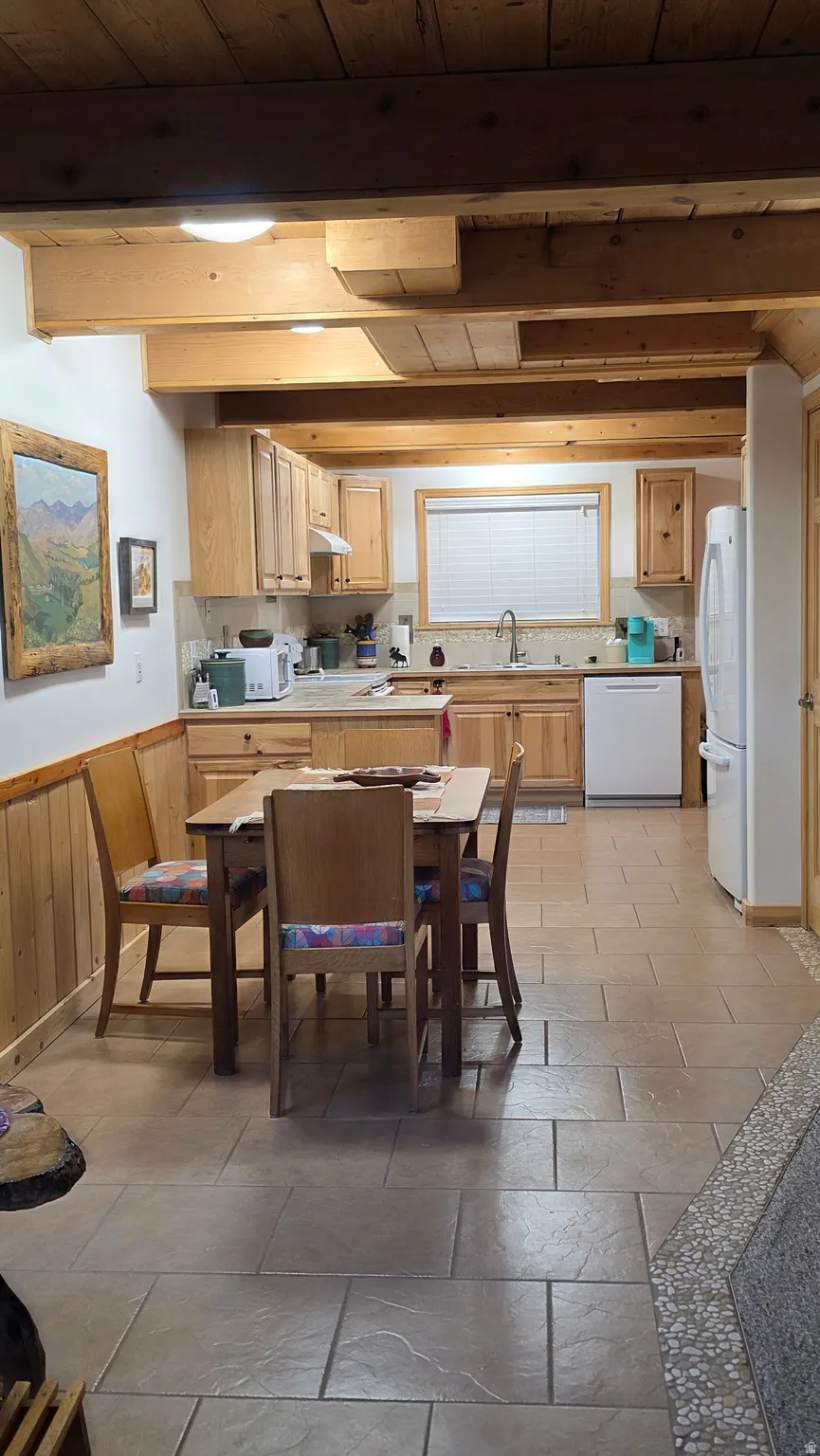 Kitchen featuring tile flooring, wood-finish cabinetry, light-toned countertops, and exposed wood ceiling beams
