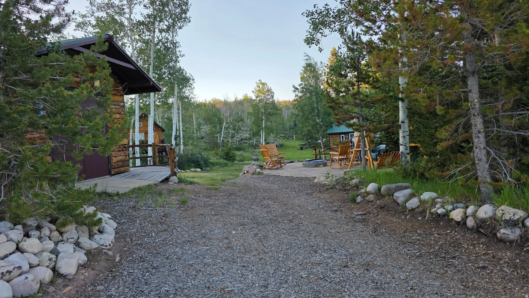 Gravel driveway leading to a log cabin exterior with a covered porch and surrounding mature trees