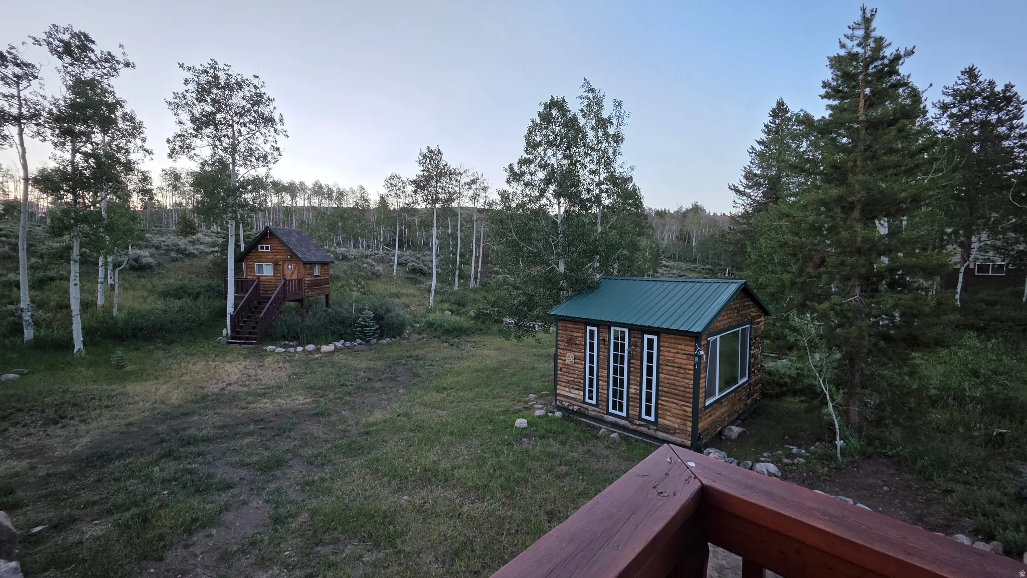 Expansive outdoor space featuring two detached structures, mature trees, and natural landscaping