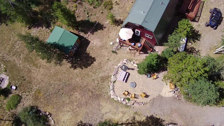 Expansive property featuring a detached outbuilding with a green metal roof, a main residence with a large elevated deck, and a distinct patio area with a fire pit