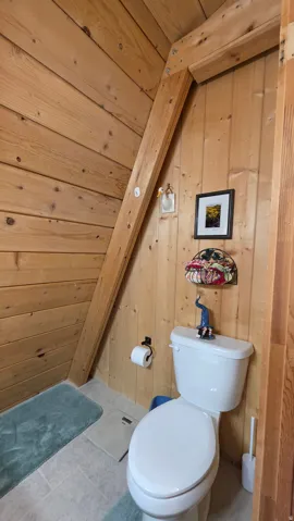 Wood-paneled bathroom featuring a white toilet, light-toned floor tiles, and a natural wood beam
