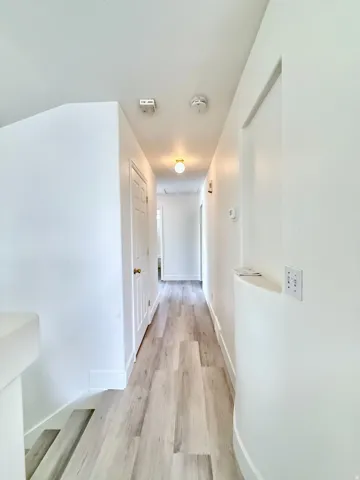 Bright hallway featuring light wood-finish flooring, white walls, and multiple panel doors