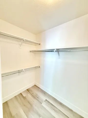 Walk-in closet featuring light wood-finish flooring, white baseboards, and multiple chrome hanging rods with shelving