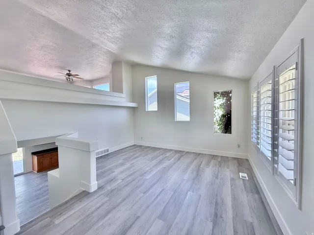 Bright living area featuring wood-finish flooring, multiple windows with plantation shutters, a vaulted ceiling, and a partial second-story overlook