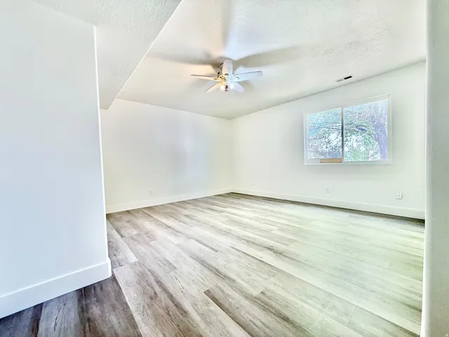 Spacious room featuring wood-finish flooring, white walls, and a ceiling fan