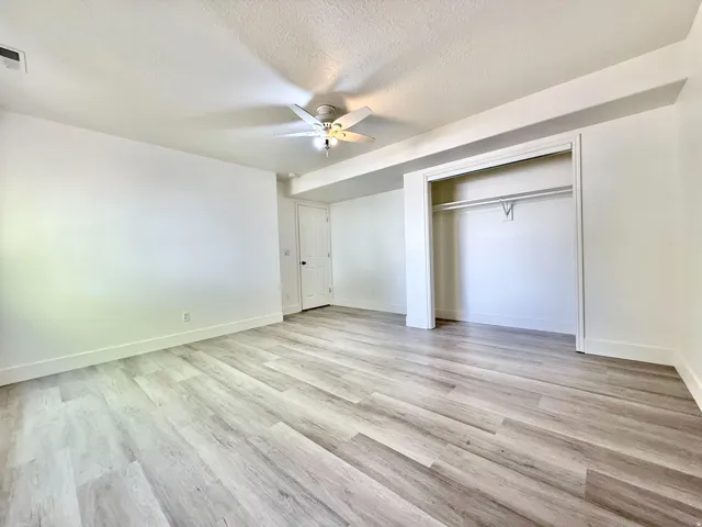 Spacious room featuring wood-finish flooring, a ceiling fan with integrated lighting, an open closet with a hanging rod, and white baseboards