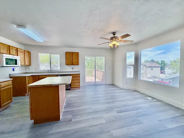 Open-concept living space featuring wood-finish flooring, a kitchen island, and a ceiling fan with integrated lighting