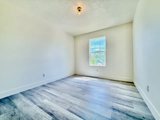 Room featuring wood-finish flooring, white walls, and a single window with white trim