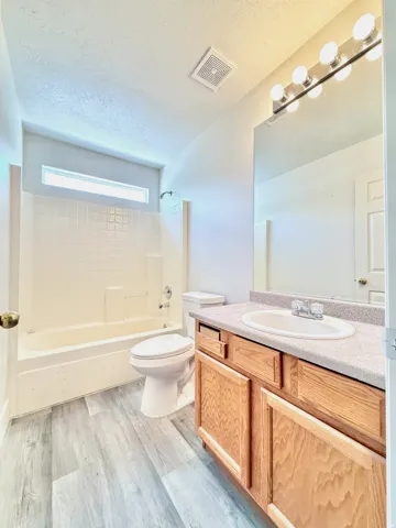 Light wood-finish vanity with a built-in sink, paired with a large mirror and multi-bulb vanity lighting