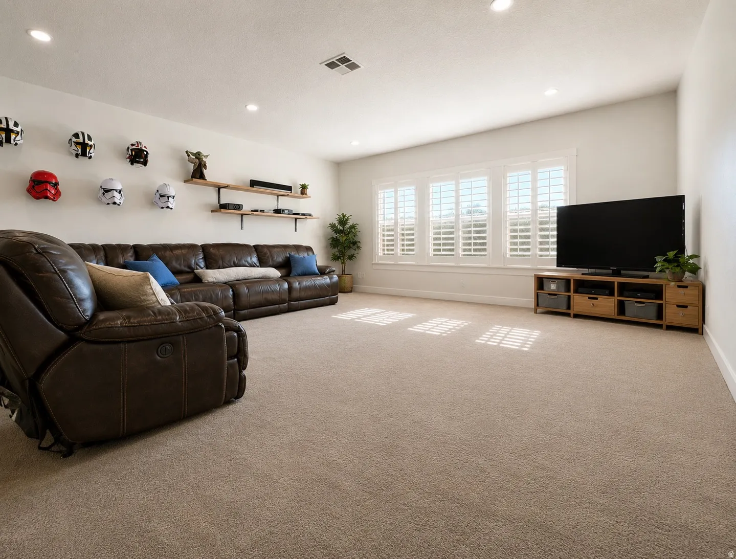 Spacious room featuring neutral carpeting, recessed ceiling lighting, and a window wall with white louvered shutters