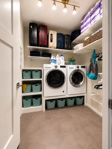 Dedicated laundry room featuring a front-loading washer and dryer, integrated shelving, and track lighting