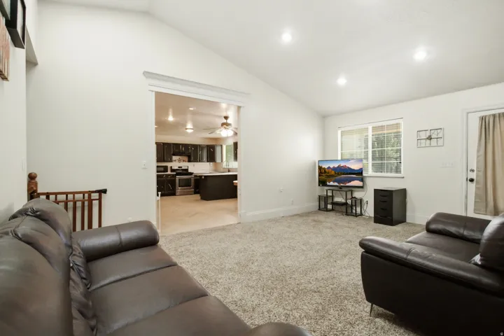 Living area featuring vaulted ceilings, recessed lighting, carpet flooring, and an expansive doorway opening to the kitchen
