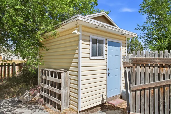 Exterior storage shed featuring horizontal siding, a light blue paneled door, and a single window