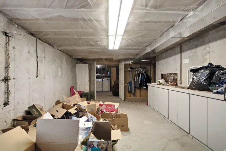 Unfinished basement with concrete walls, exposed ceiling joists, and fluorescent lighting