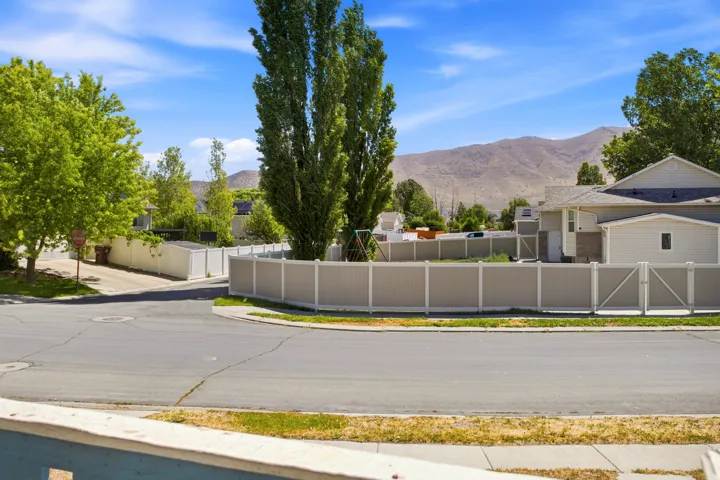 Fenced property featuring a large yard with mature trees, paved street frontage, and mountain backdrop