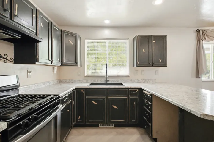 U-shaped kitchen layout featuring black shaker-style cabinetry, a stainless steel range with overhead ventilation, and light-toned countertops