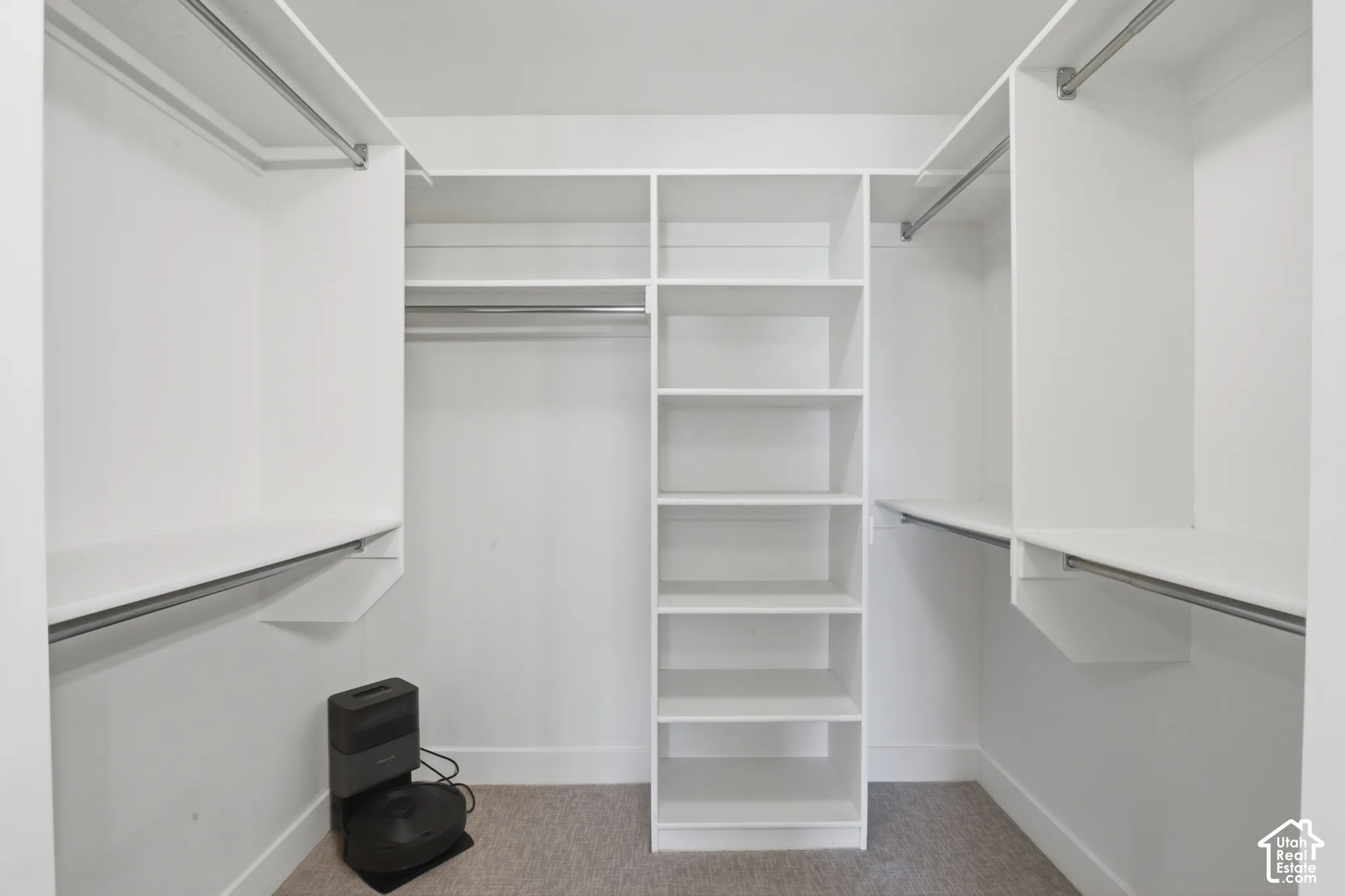 Primary bedroom walk-in closet featuring white built-in shelving, multiple hanging rods, and light-colored carpeting