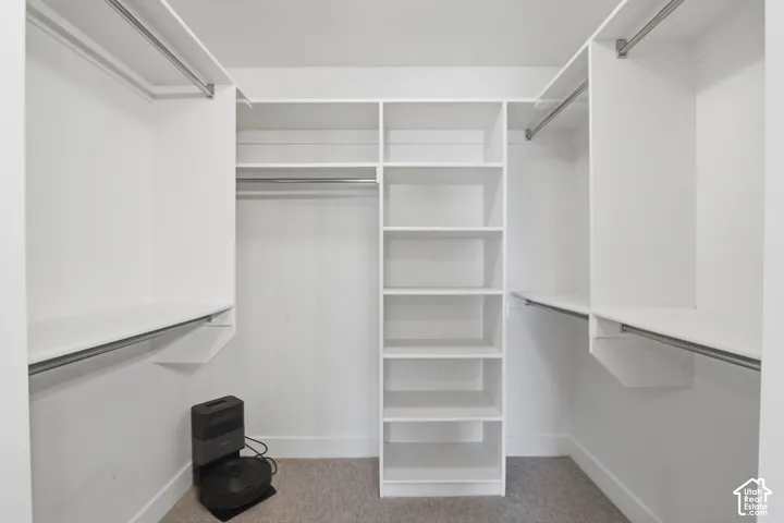 Primary bedroom walk-in closet featuring white built-in shelving, multiple hanging rods, and light-colored carpeting